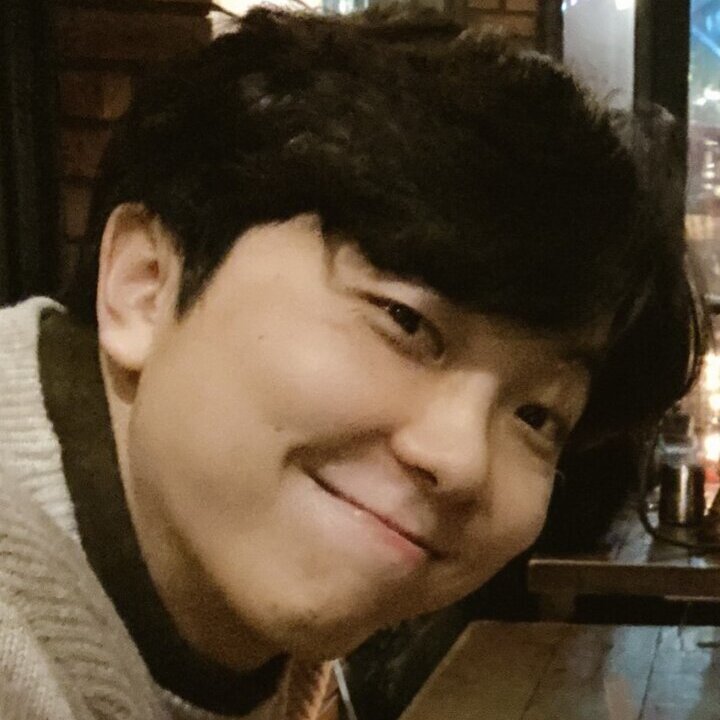 Seungchul's head takes up most of the area of the photo--no teeth smirk-smile--looks to be inside an office